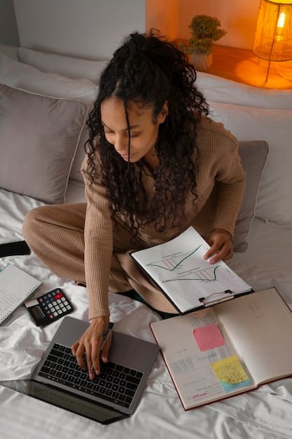 A person using a calculator and reviewing a budget spreadsheet on a laptop. The scene is brightly lit, with financial documents and graphs visible in the background, highlighting the task of financial planning.