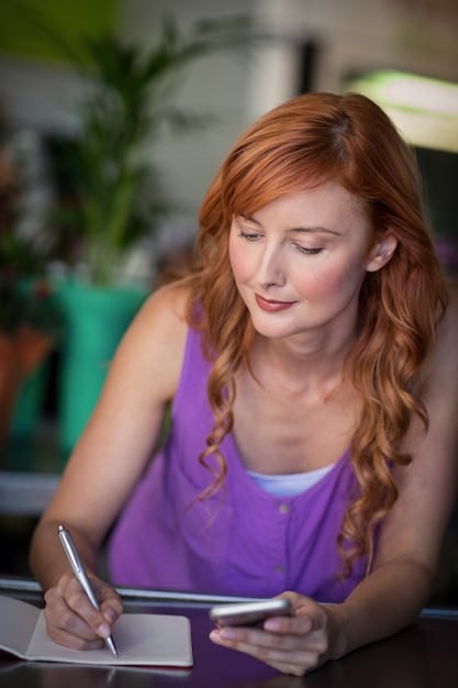 A woman looking thoughtfully at her credit card statement, highlighting specific expenses with a marker. She has a notepad nearby with handwritten notes.
